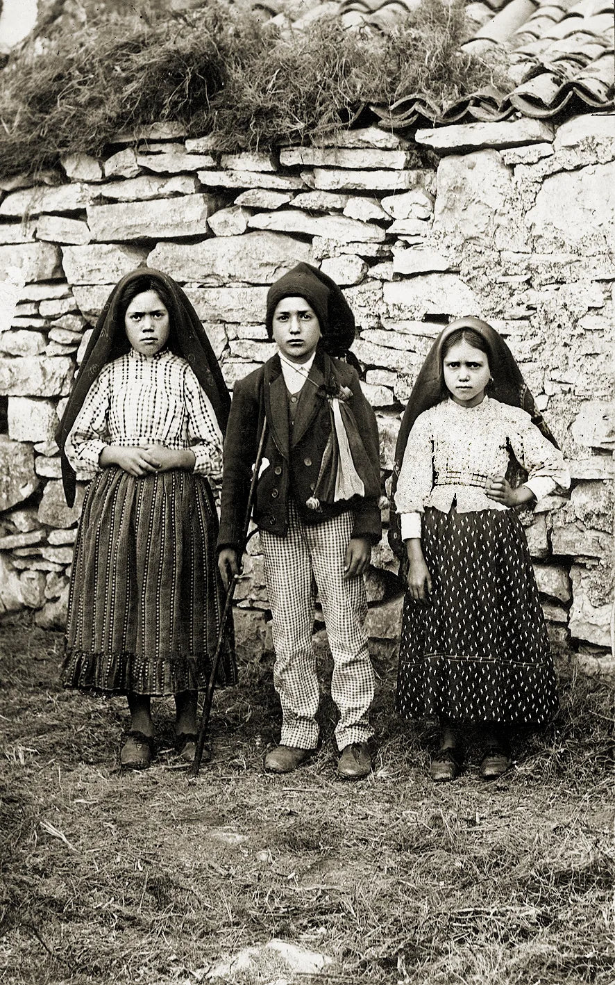 Historic photograph of the three shepherd children of Fátima beside a stone wall